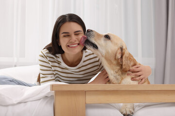 Happy woman with cute Labrador Retriever on bed at home