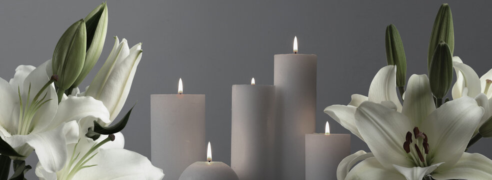 Funeral. Burning candles between white lilies on grey background, banner design