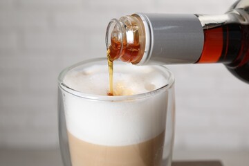 Pouring syrup into glass of tasty coffee on blurred background, closeup