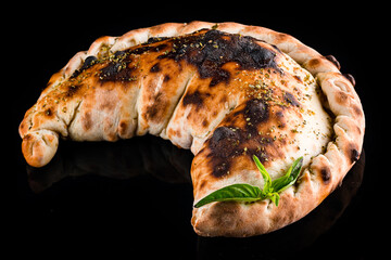 Lunch Neapolitan closed pizza calzone with basil and spices isolated on black.