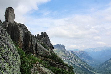 Obraz premium View from the hill to the hollow between mountains and rock. Summer mountain landscape. Green pine forest, hight peaks
