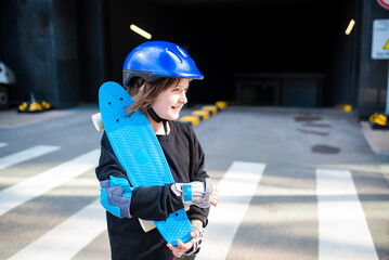 portrait of happy schoolboy in purple helmet, holding blue urban cruiser, skateboard.