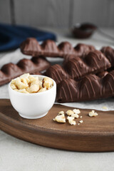 Sweet tasty chocolate bars on light table, focus on bowl with hazelnuts
