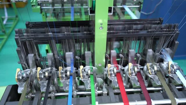 Thread from weaving machine. The mechanical equipment of the plastic weaving production line is running in a factory. Industrial narrow woven production line. Weaving looms in a textile factory.