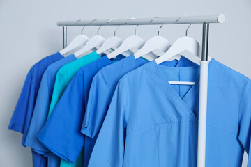 Different medical uniforms on rack against light grey background