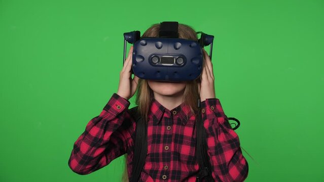 Portrait of a happy teenage girl with long hair in a VR headset, she looks around in virtual reality on a green screen. Replacing the background. Chroma key.