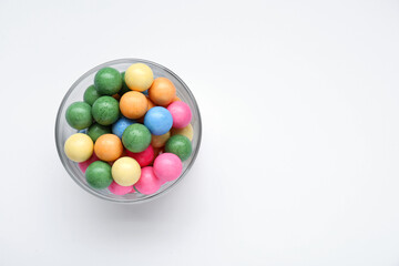 Fototapeta na wymiar Bowl with many bright gumballs on white background, top view. Space for text