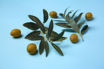 Fresh olives and green leaves on light blue background, closeup