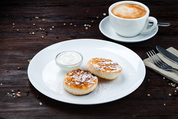 Cheese pancakes with sour cream, powdered sugar and cup of coffee.