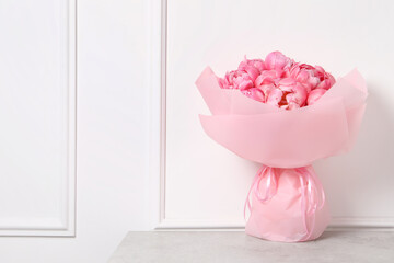 Bouquet of beautiful pink peonies on table near white wall. Space for text