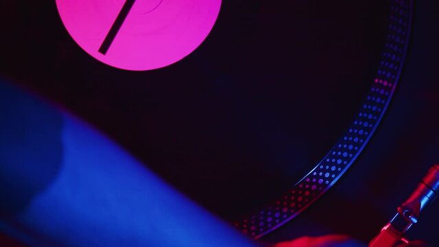 DJ carefully places the headshell of the turntable on the record and turns on the playback during the studio recording of the vinyl session in a color light close up