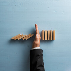 Overhead view of hand in a business suit stopping or intervening collapsing dominos