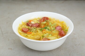 Delicious sauerkraut soup with smoked sausages and green onion on light grey table