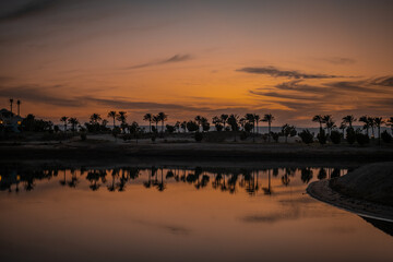 Sonnenuntergang an der Lagune bei Ancient Sands in El Gouna, Ägypten. Die LAndschaft mit den Plamen und Häusern spiegelt sich im Wasser.