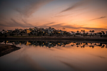 Fototapeta premium Sonnenuntergang an der Lagune bei Ancient Sands in El Gouna, Ägypten. Die LAndschaft mit den Plamen und Häusern spiegelt sich im Wasser.