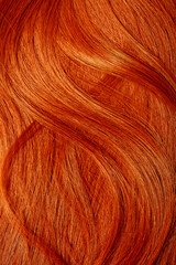 Red hair close-up as a background. Women's long orange hair. Beautifully styled wavy shiny curls. Hair coloring bright shades. Hairdressing procedures, extension.