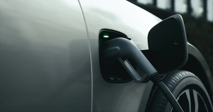 CU shot of generic EV hybrid vehicle is charging on a station, view of charger plugged into socket