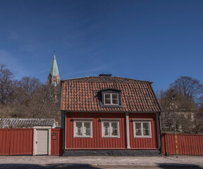 Old wood red house at the foot of a hill with the church Sofia in background, a sunny spring day in Stockholm