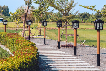 Fototapeta premium Beautiful view of outdoor lamps on walkway for garden lighting in summer park. Pathway in park with the light pole. Wood lantern on an pole. An outdoor park for rest and relaxation. Selective focus.