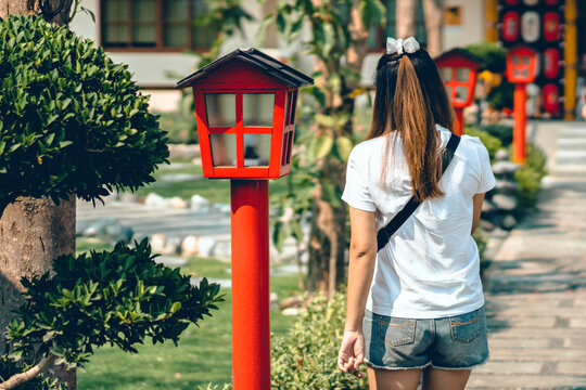 Back view of Asian young woman using smartphone to take a photo with beautiful of Japanese garden with red lanterns between the walkways. Happiness people with outdoor park for rest and relaxation.