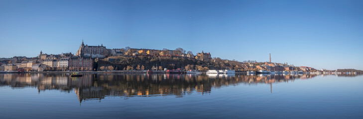 Fototapeta na wymiar Pier Södermälastrand, cliffs Mariaberget, Skinnarviksberget, old 1700s houses brick factory building, waterfront, cargo, fish and hotels ships, a tranquil sunny spring day, Stockholm Sweden 2023-04-21