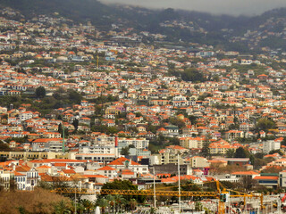 Obraz premium The sprawling hillside town of Funchal, the capital of Madeira, under a cludy grey sky 