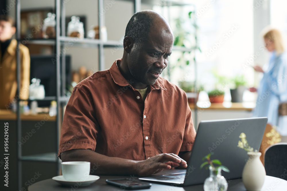 Aufkleber mature african american businessman typing on laptop keyboard while sitting by table in cafe, having