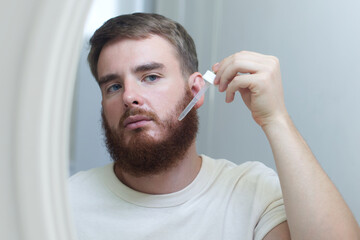 young handsome bearded man apply serum oil, cosmetic product, lotion for healthy perfect fresh skin...