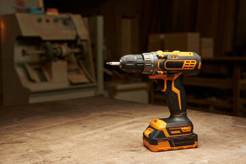 a cordless electric drill stands on a wooden table against the background of a woodworking workshop...