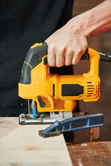 Fototapeta premium The hand of a Caucasian worker saws a wooden board with an electric jigsaw. chips fly