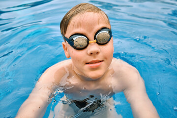 Naklejka premium Smiling boy portrait in swimming goggles, Child swim in the pool, sunbathes, swimming in hot summer day. Relax, Travel, Holidays, Freedom concept. 