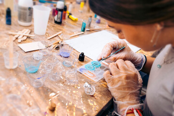 Jewelry workshop with epoxy resin. Close-up of a woman's gloved hands using jewelry tongs.