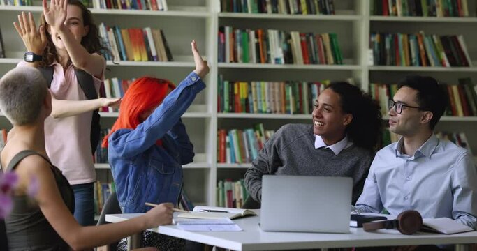 Pretty student girl with backpack goes to library, greeting schoolmates, gives high five gesture glad to see multi ethnic friends, gathered to do joint task, prepare for exams. Relations, education