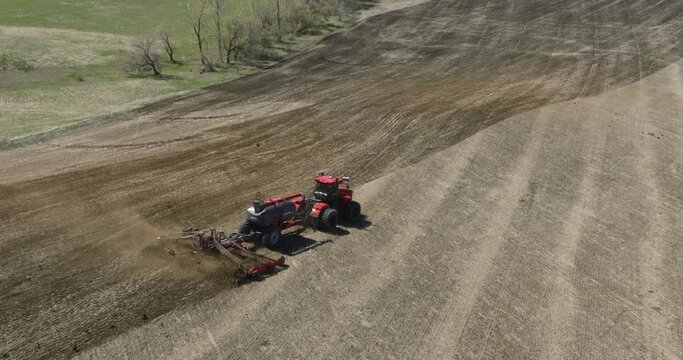 Field works. Tractor sowing seeds with seeder driller in field. Process of sowing cereals and other crops. Sowing work in the field. Tractor with seeder performing seeding. Top down drone view.