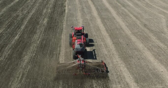 Field works. Tractor sowing seeds with seeder driller in field. Process of sowing cereals and other crops. Sowing work in the field. Tractor with seeder performing seeding. Top down drone view.