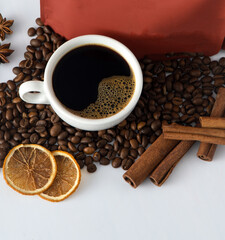 White cup of coffee top view. Coffee beans and packing bag. An invigorating drink in the morning for breakfast. Food background. Copy space banner. Сinnamon sticks and dried orange.