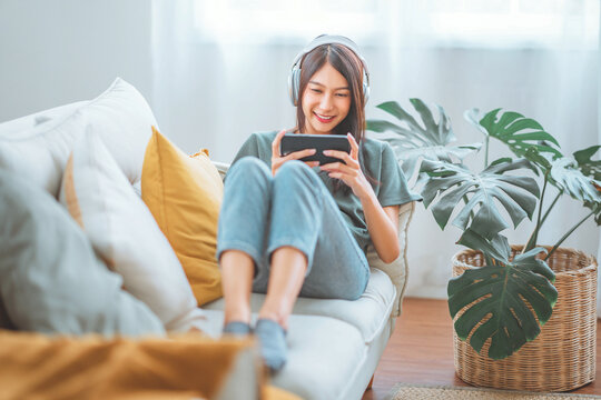 Happy asian woman listening to music from mobile phone while sitting on the sofa at homes, Smiling girl relaxing with headphones in morning, Time to relax.