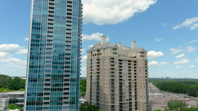panning aerial footage of glass skyscrapers, office buildings and condominiums with lush green trees and cars on the street, a gorgeous blue sky with clouds in Buckhead in Atlanta Georgia USA