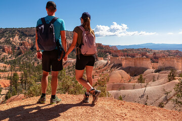 Couple holding hands with scenic aerial view from Fairyland hiking trail on massive hoodoo sandstone rock formations, Bryce Canyon National Park, Utah, USA. Unique natural landmark in barren landscape - Powered by Adobe