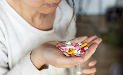 Woman's hand hold many medicine, boxes of medicines in the background.