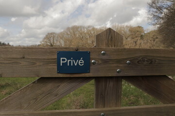 Private sign on wooden gate in front of green field and forest. The Dutch word 'Privé' means Private. 