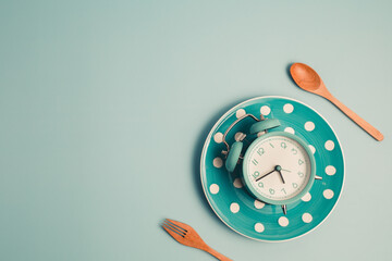 An alarm clock on an empty plate and cutlery set