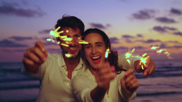 Young latin couple playing sparklers on beach at sunset. They having fun dancing enjoying holiday on the beach.