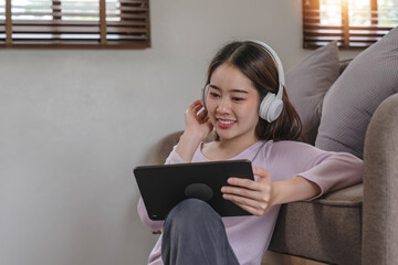 Confident asian woman listening to music with earphones and use tablet while relaxing of work in the office at home.