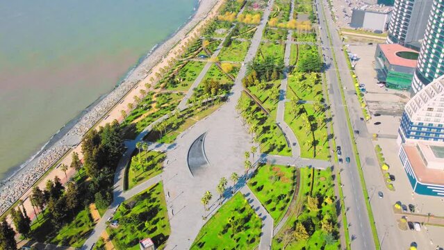 Resort town of Batumi in Georgia. Aerial view of green park on sunny day against background of sea. Lehi and Maria Kaczynski Park in city. Beautiful green landscaping. Infrastructure, mountains