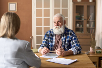 Serious senior man talking to financial advisor during their meeting at table with documents at home