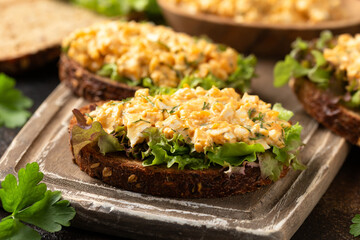 Egg salad sandwiches with greens and herbs on wooden board. Healthy food.