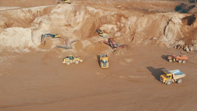 Quarry dump truck unloads the rock into a rock crusher. Open pit mine quarrying extractive industry stripping work. Conveyor and production of construction gravel and sand.