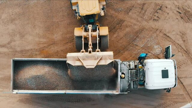Aerial top down view of an excavator loading crushed stone into a dump truck in a crushed stone quarry