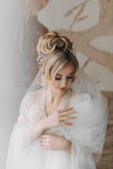 A bride with an elegant hairstyle, in a robe, stands looking down and holding her snow-white veil...